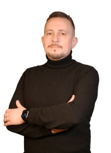 Man with short hair and goatee wearing a black turtleneck, arms crossed, looking at the camera.